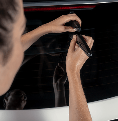 Nahaufnahme der Hände eines Technikers, der ein Kia Original-Wischerblatt an der Heckscheibe eines Fahrzeugs montiert. Die Scheibe spiegelt die Szene.